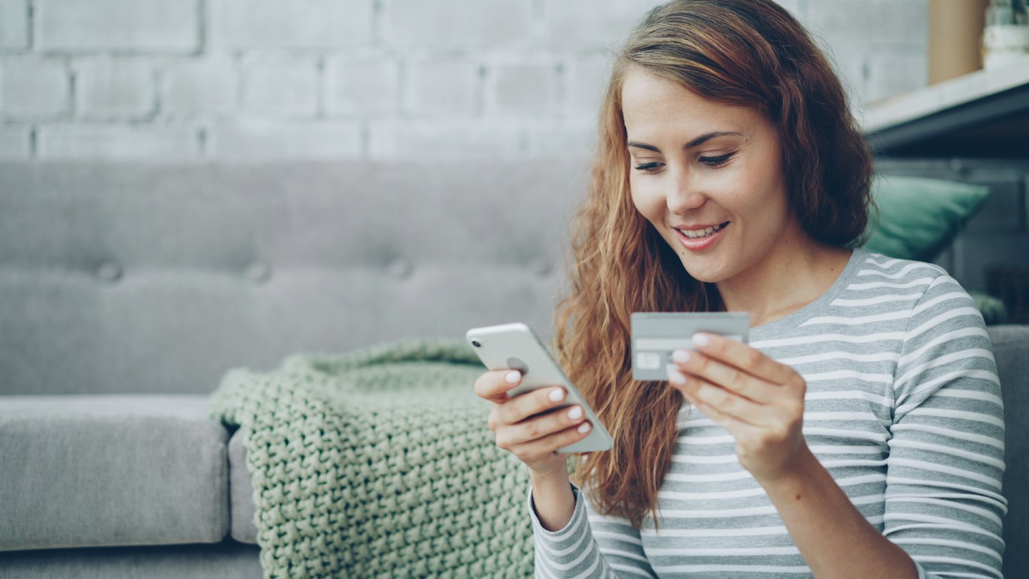 Woman smiles while holding phone and credit card shopping online.